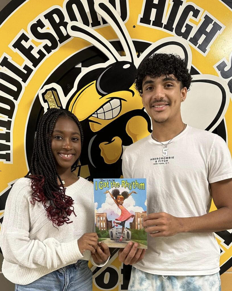 Two teenage students holding a copy of a children's book titled I Got Rythm