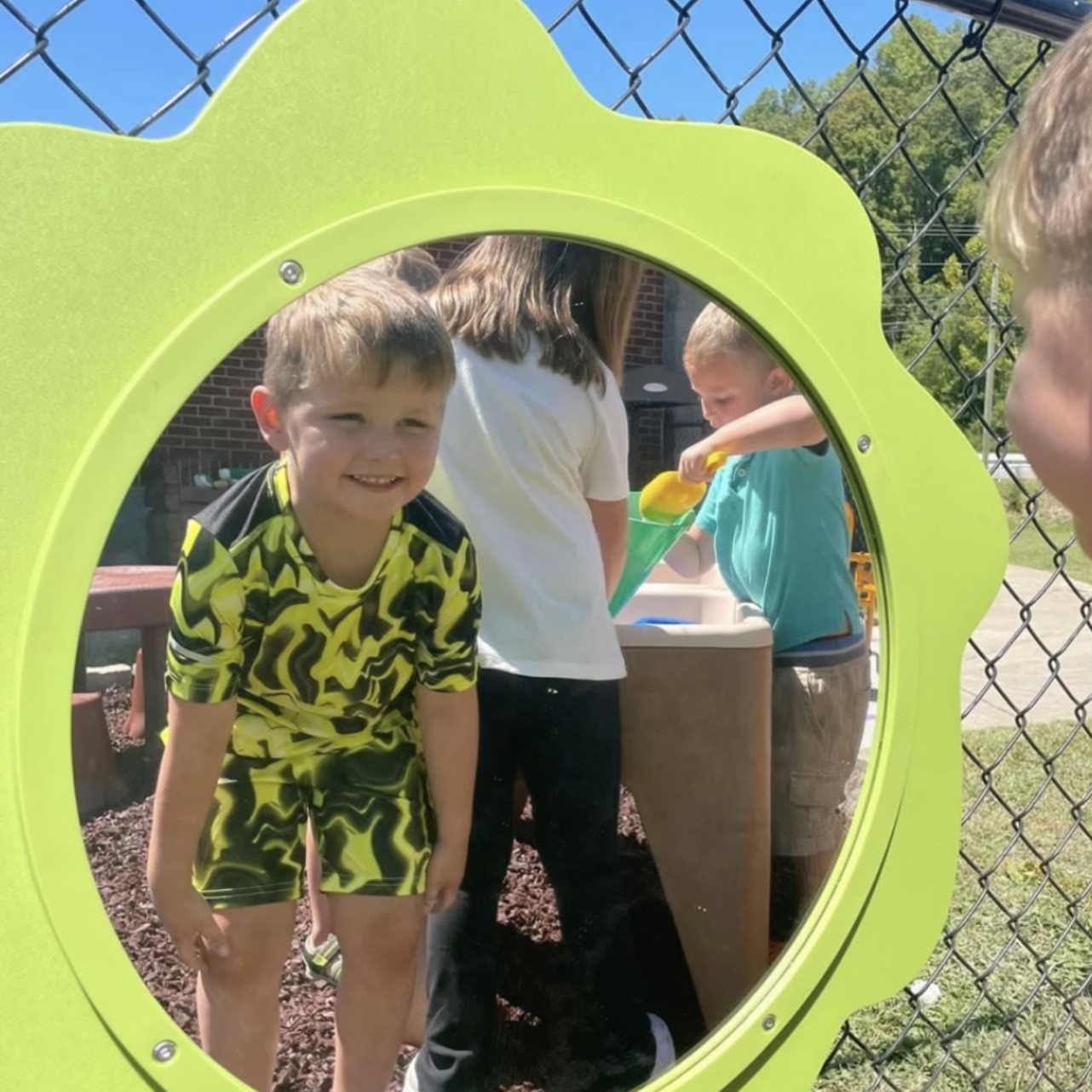 a young boy smiles into a mirror on a playground